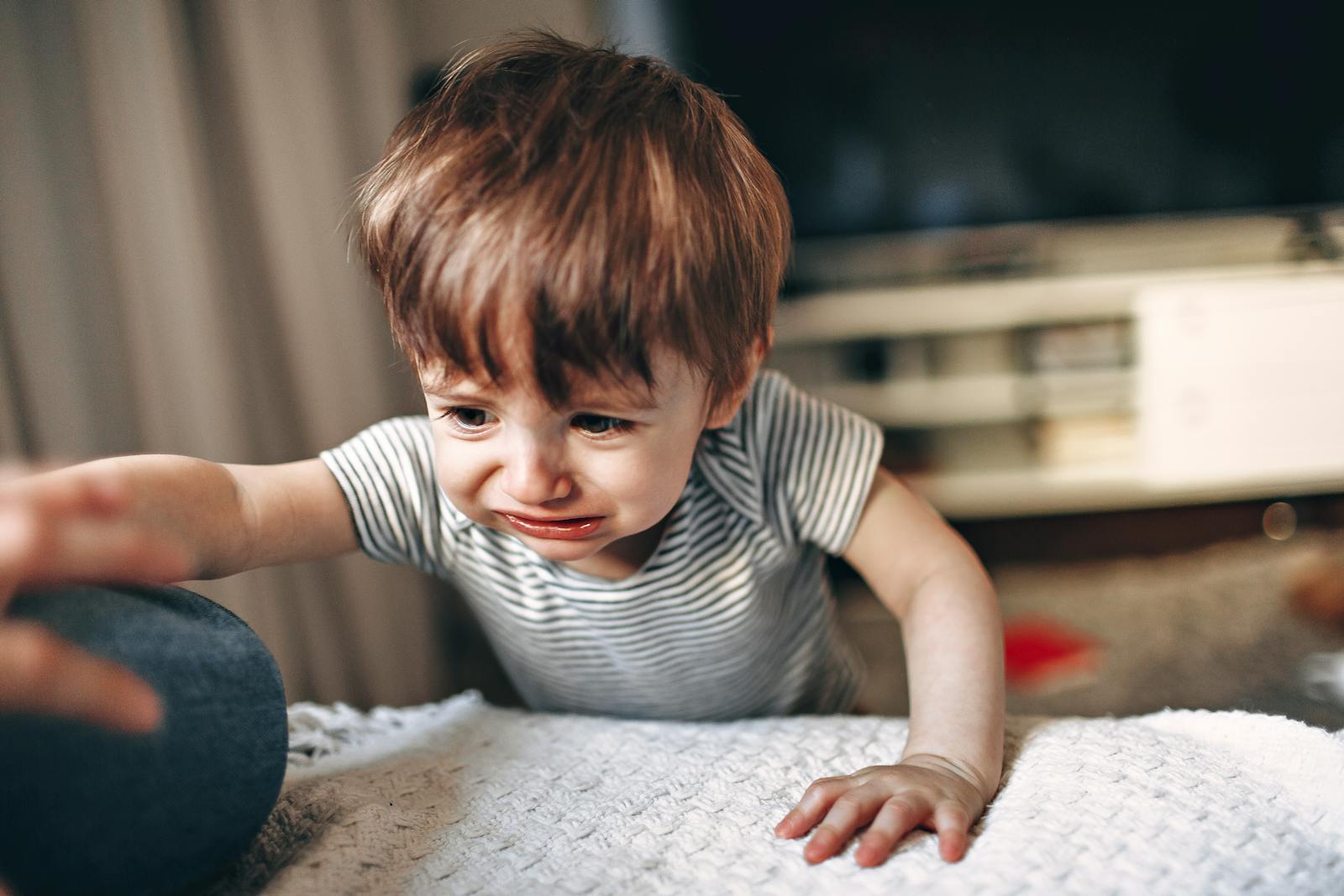 Parent gently helping an upset child settle on the sofa
