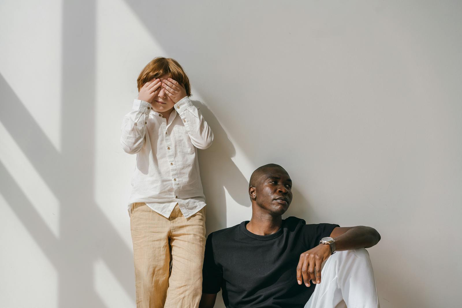 Parent and child sitting together against a sunlit wall